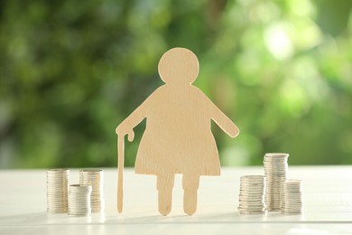 Pension savings. Figure of senior woman and stacked coins on white wooden table outdoors