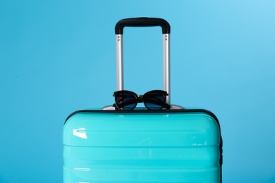 Stylish suitcase with sunglasses on color background