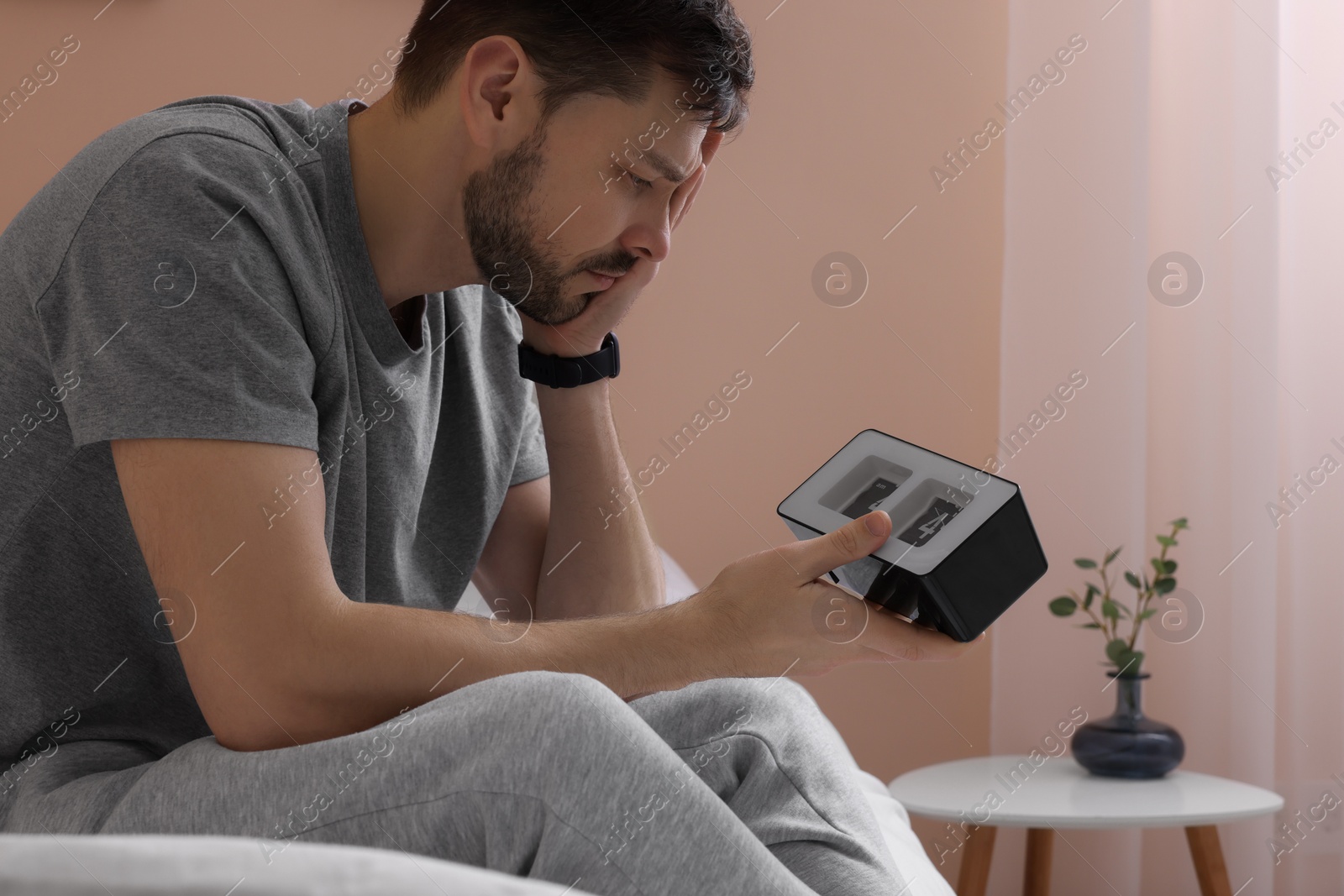 Photo of Sleepy man with clock in bed at home, closeup