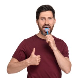 Handsome man brushing his tongue with cleaner and showing thumb up on white background
