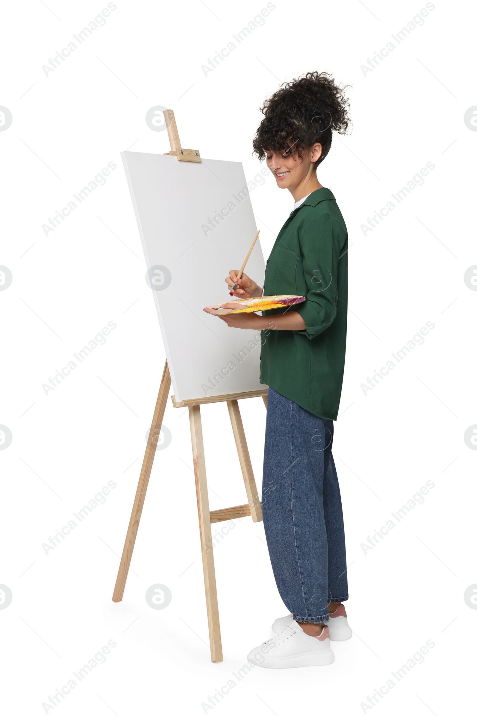 Photo of Young woman painting on easel with canvas against white background