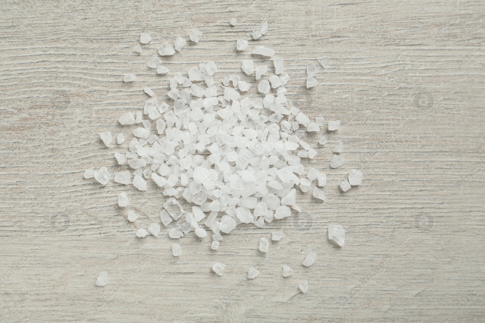 Photo of Natural sea salt on light wooden table, flat lay