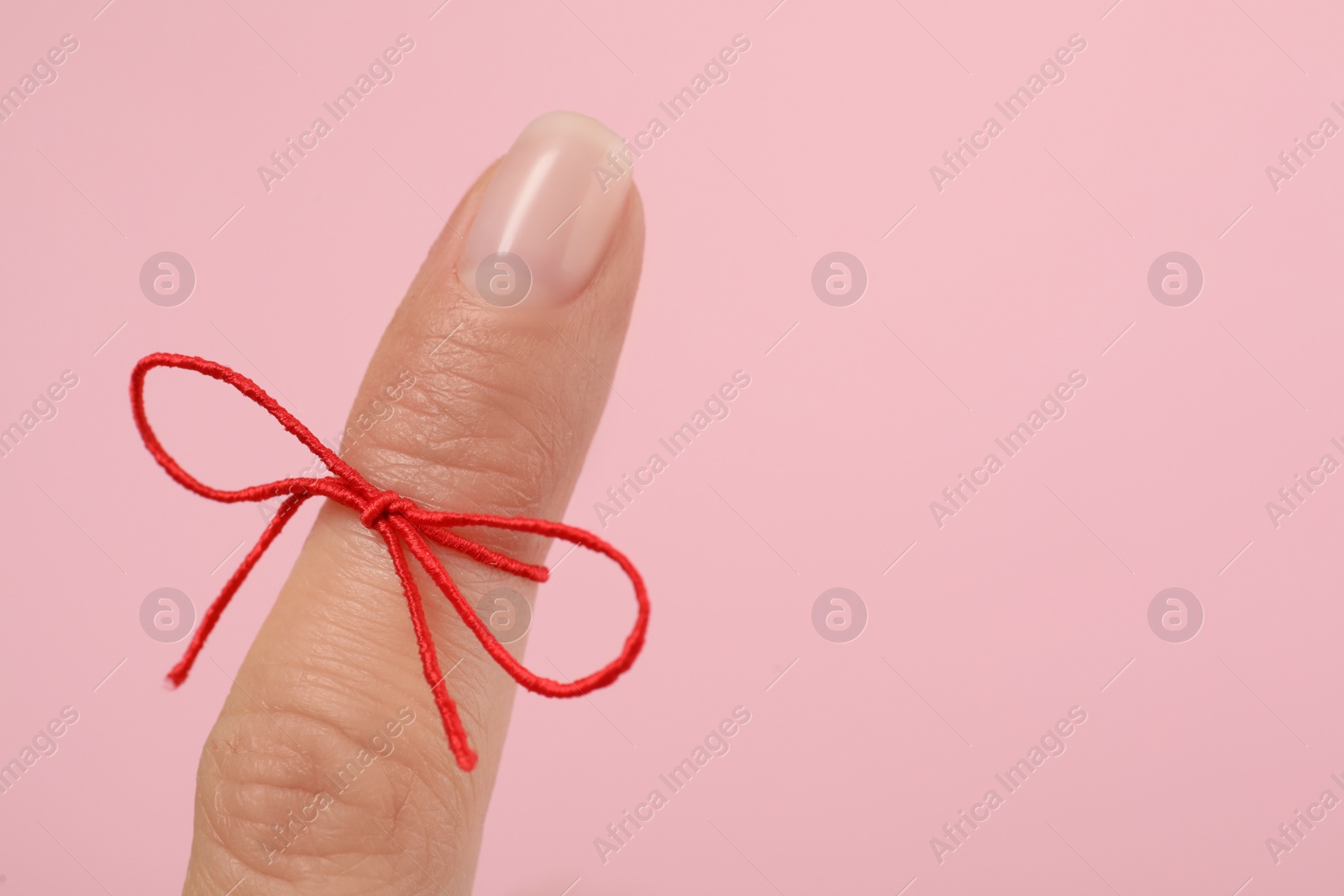 Photo of Woman showing index finger with tied red bow as reminder on pink background, closeup, Space for text