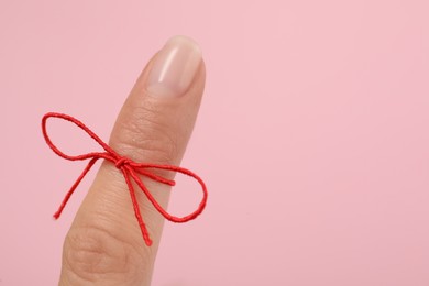 Photo of Woman showing index finger with tied red bow as reminder on pink background, closeup, Space for text