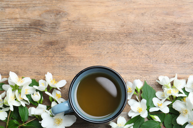 Cup of tea and fresh jasmine flowers on wooden table, flat lay. Space for text