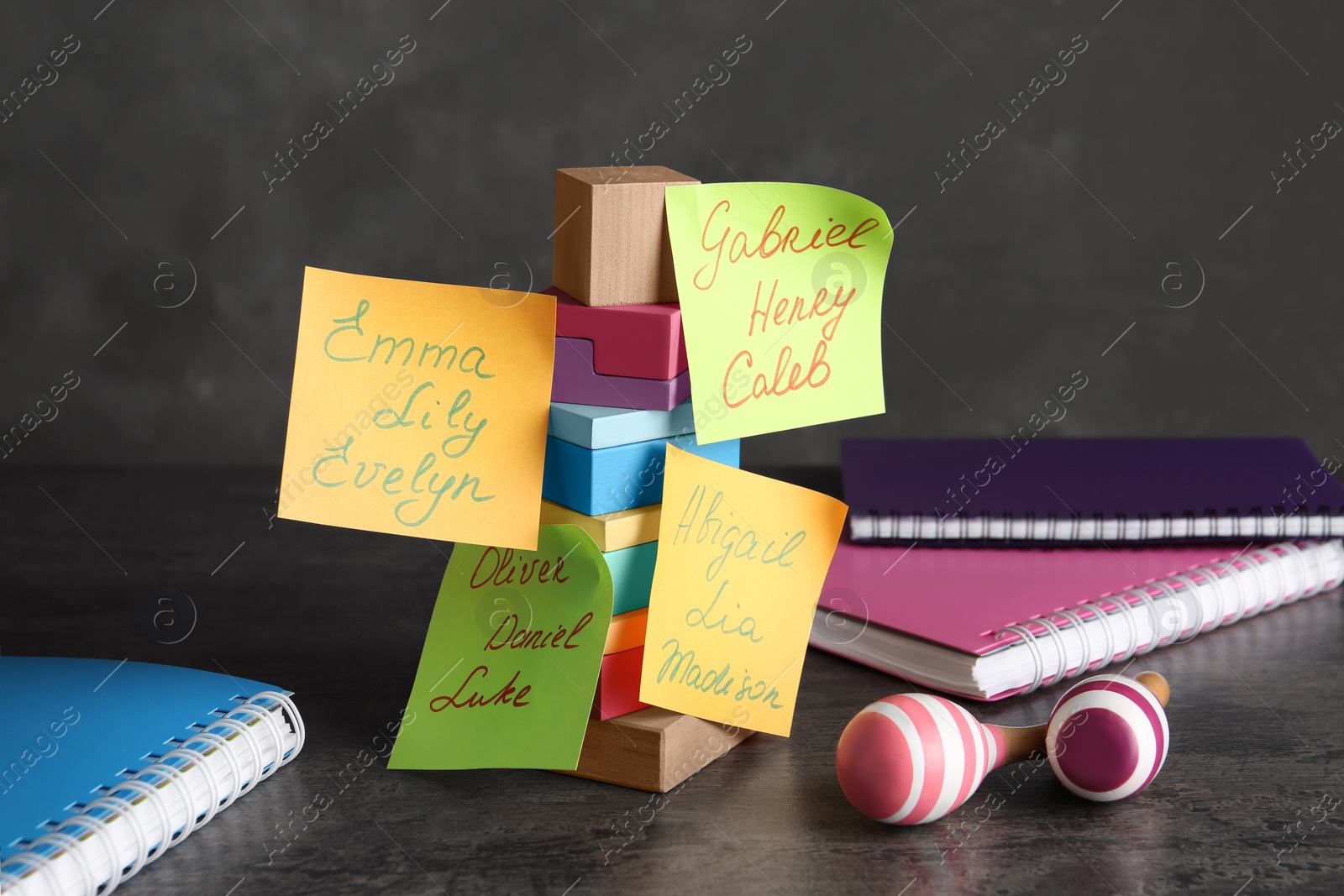 Photo of Paper notes with different baby names, toys and notebooks on grey table