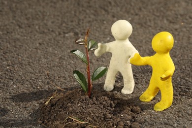 Human figures with soil and green seedling on asphalt road