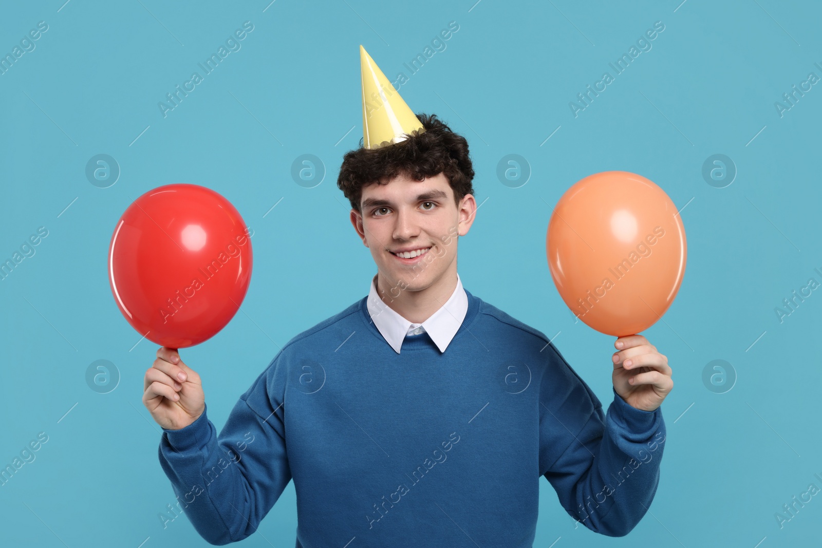 Photo of Young man in party hat with balloons on light blue background