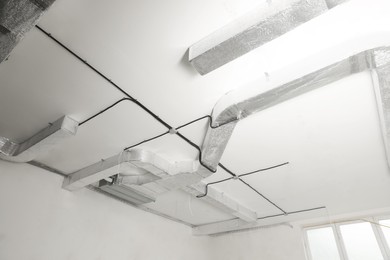 Conduits with cables and ventilation system on white ceiling, low angle view. Installation of electrical wiring