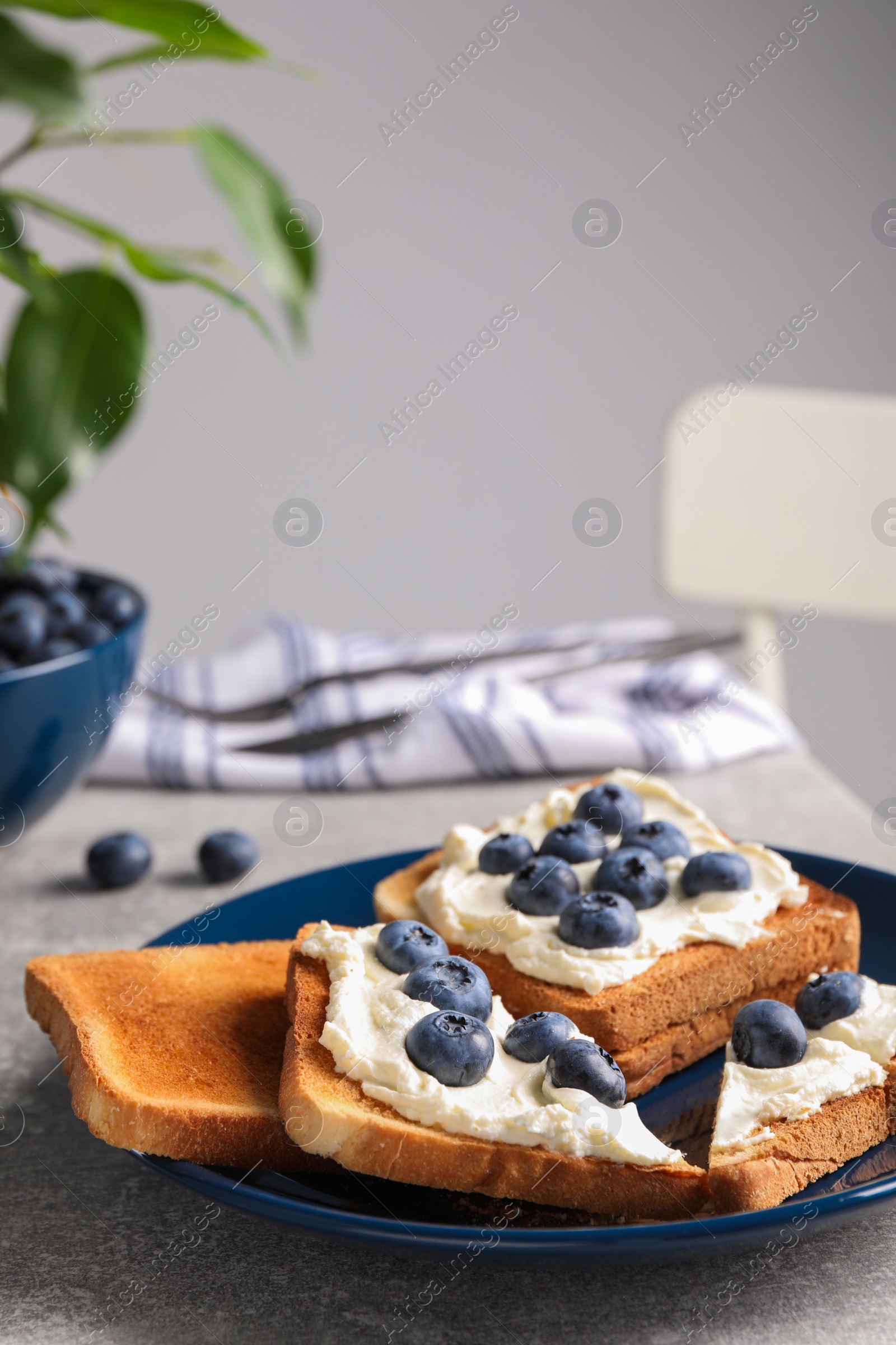 Photo of Tasty sandwiches with cream cheese and blueberries on grey table indoors