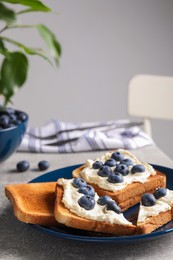 Tasty sandwiches with cream cheese and blueberries on grey table indoors