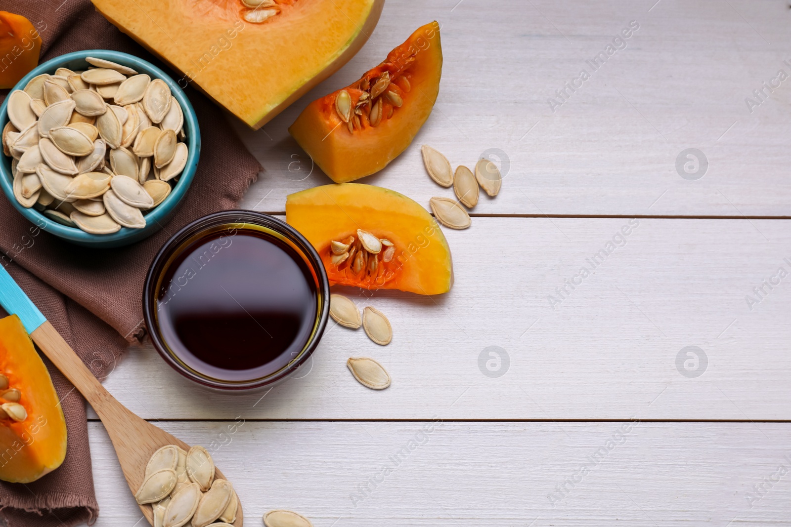 Photo of Flat lay composition with glass bowl of pumpkin seed oil on white wooden table. Space for text