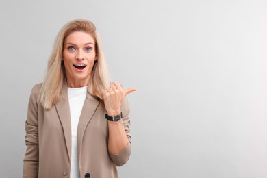 Portrait of emotional middle aged businesswoman pointing at something on light grey background. Space for text