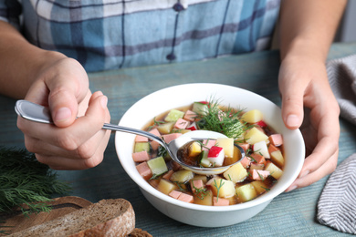 Photo of Woman eating delicious cold okroshka with kvass at blue wooden table, closeup. Traditional Russian summer soup