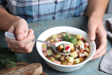 Woman eating delicious cold okroshka with kvass at blue wooden table, closeup. Traditional Russian summer soup