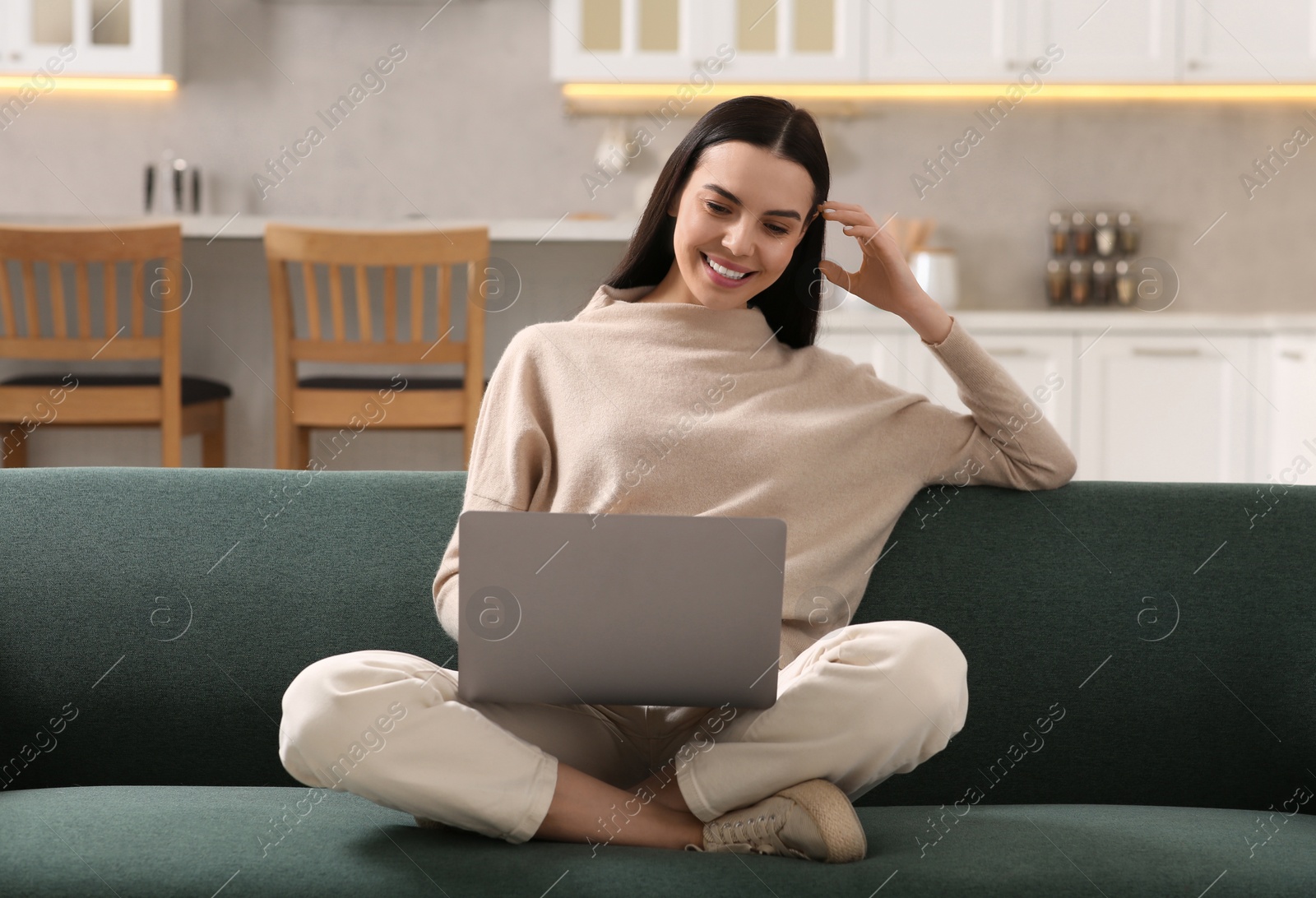 Photo of Happy woman working with laptop on sofa in kitchen