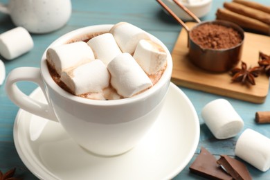 Photo of Tasty hot chocolate with marshmallows and ingredients on light blue wooden table, closeup