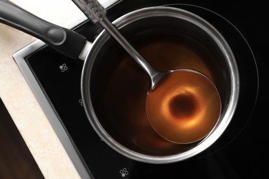 Saucepan and ladle with used cooking oil on stove, top view