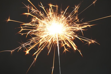 Photo of Bright burning sparkler on black background, closeup