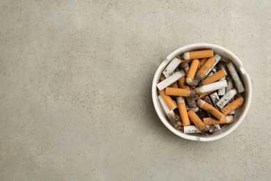 Photo of Ceramic ashtray full of cigarette stubs on grey table, top view. Space for text