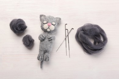 Felted cat, wool and needles on light wooden table, flat lay