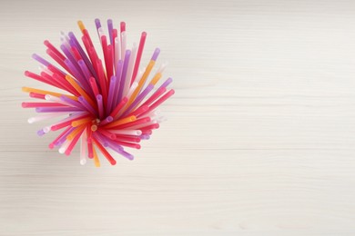 Photo of Colorful plastic drinking straws on white wooden table, top view. Space for text