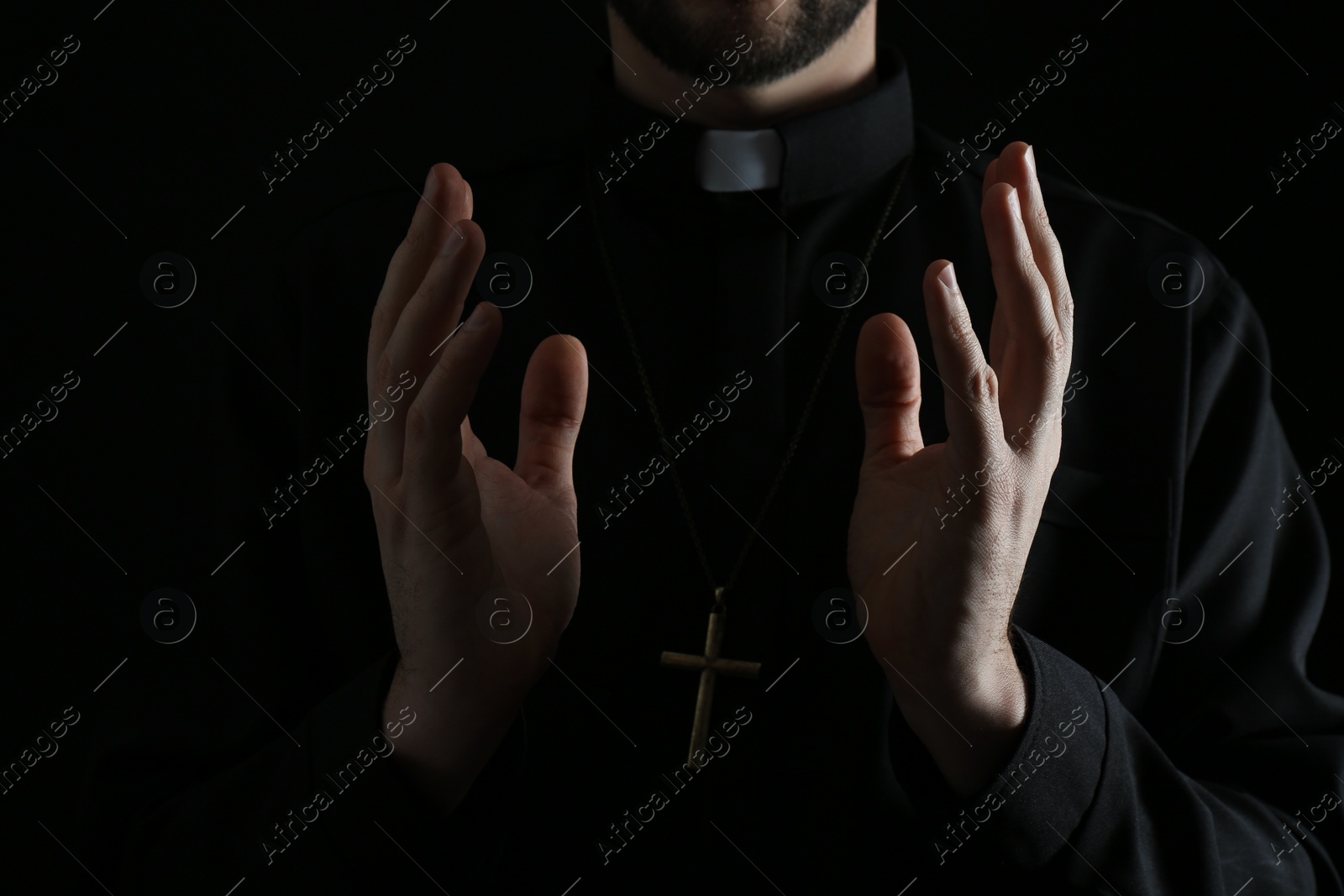 Photo of Priest in cassock praying on dark background, closeup