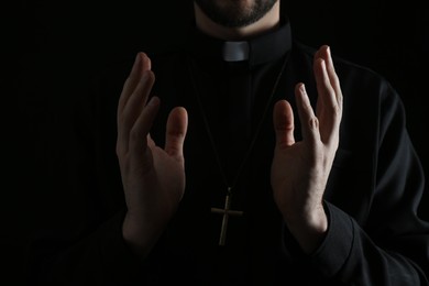 Priest in cassock praying on dark background, closeup