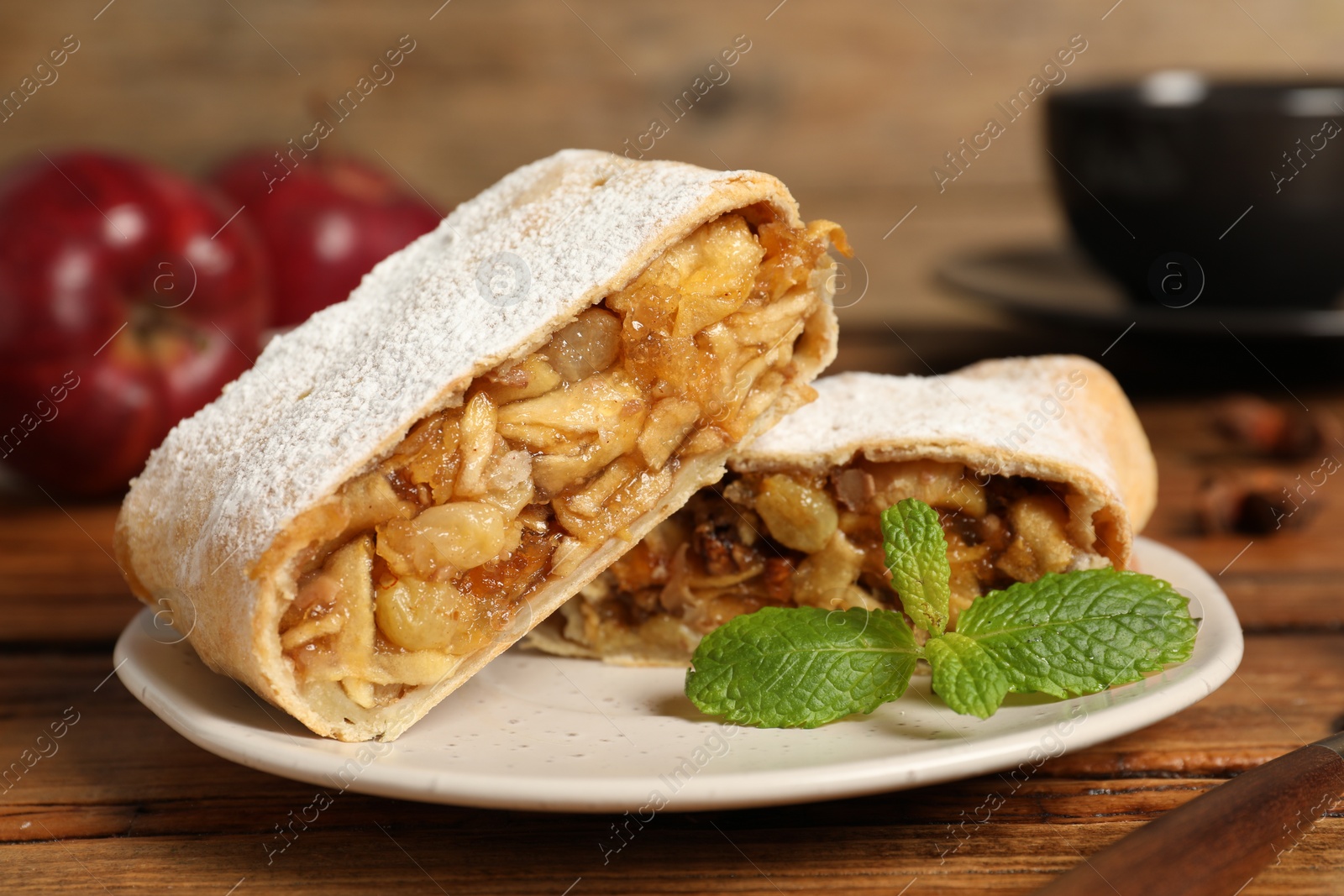 Photo of Delicious strudel with apples, nuts and raisins on wooden table, closeup
