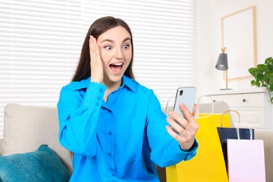 Special Promotion. Emotional woman with smartphone on sofa indoors