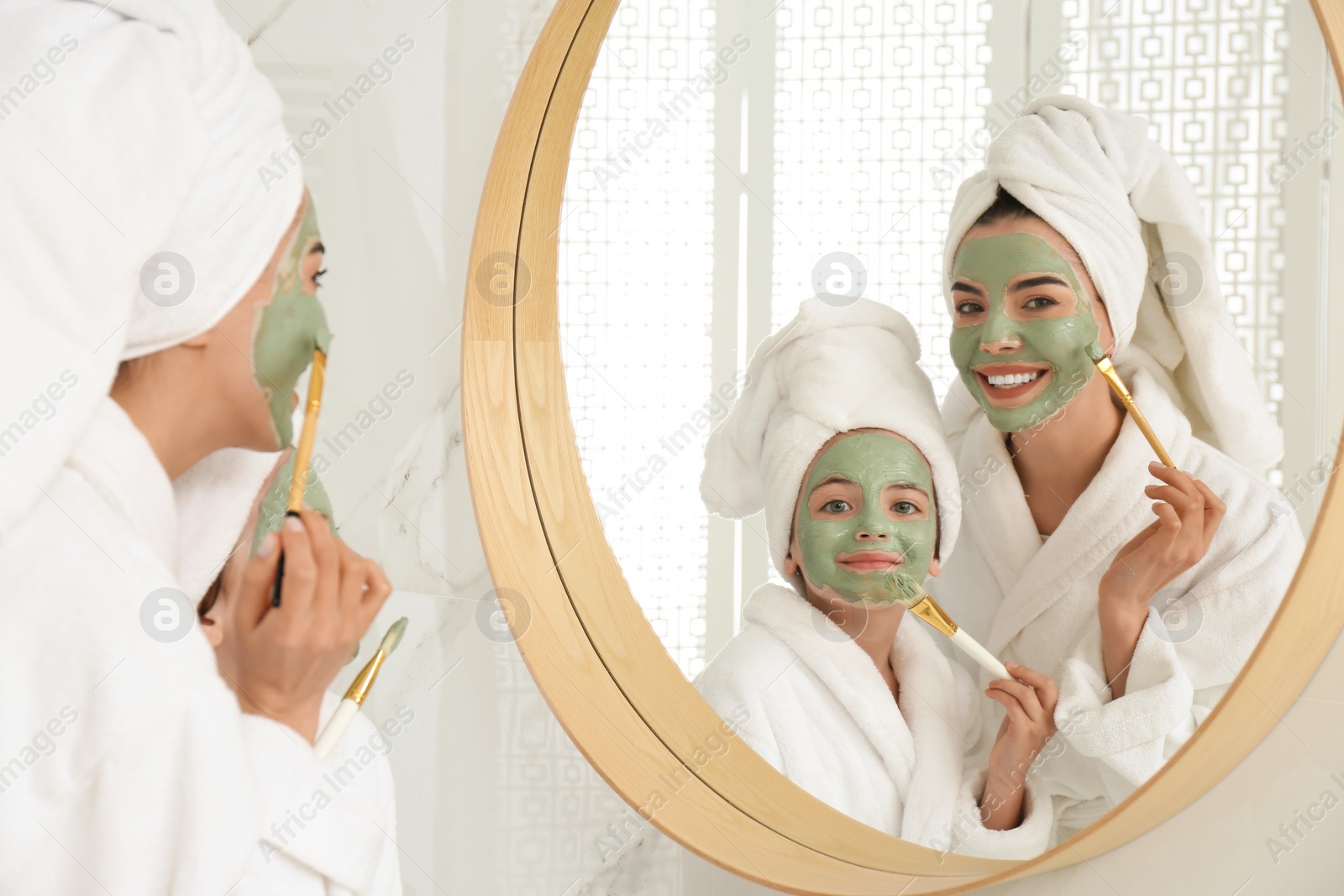 Photo of Young mother and her daughter with facial masks near mirror in bathroom