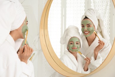 Photo of Young mother and her daughter with facial masks near mirror in bathroom