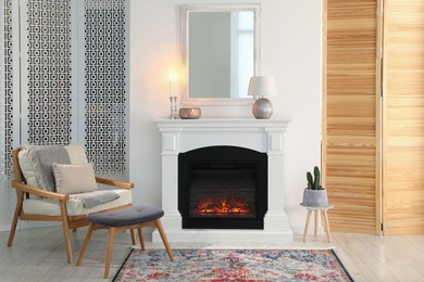 Photo of Beautiful fireplace, armchair and ottoman in living room. Interior design