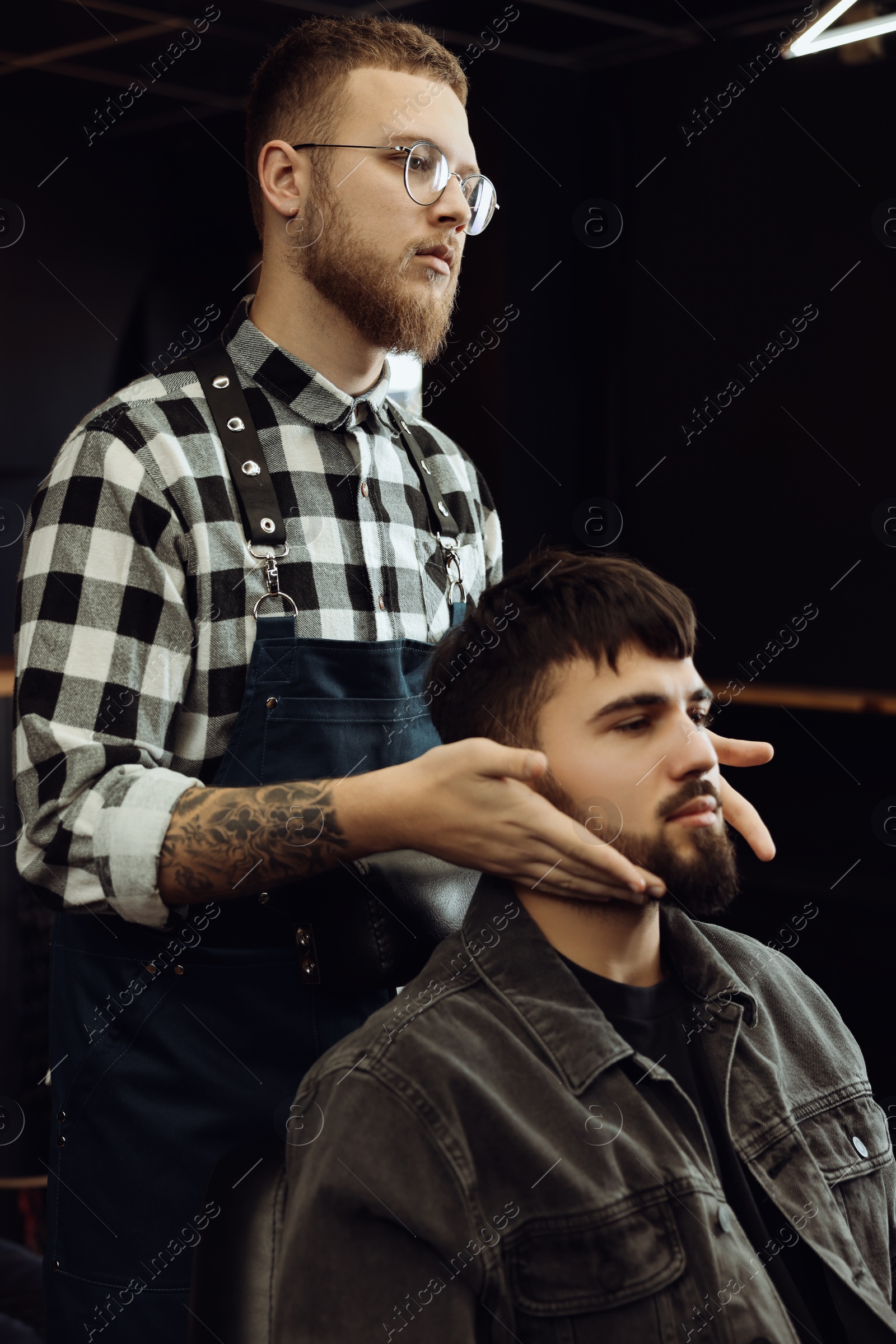 Photo of Professional hairdresser working with bearded client in barbershop