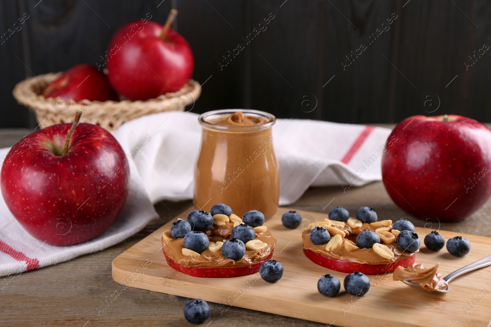 Photo of Slices of fresh apple with peanut butter and blueberries on wooden table