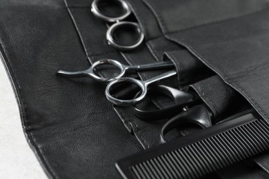 Hairdresser tools. Professional scissors and comb in leather organizer on white table, closeup