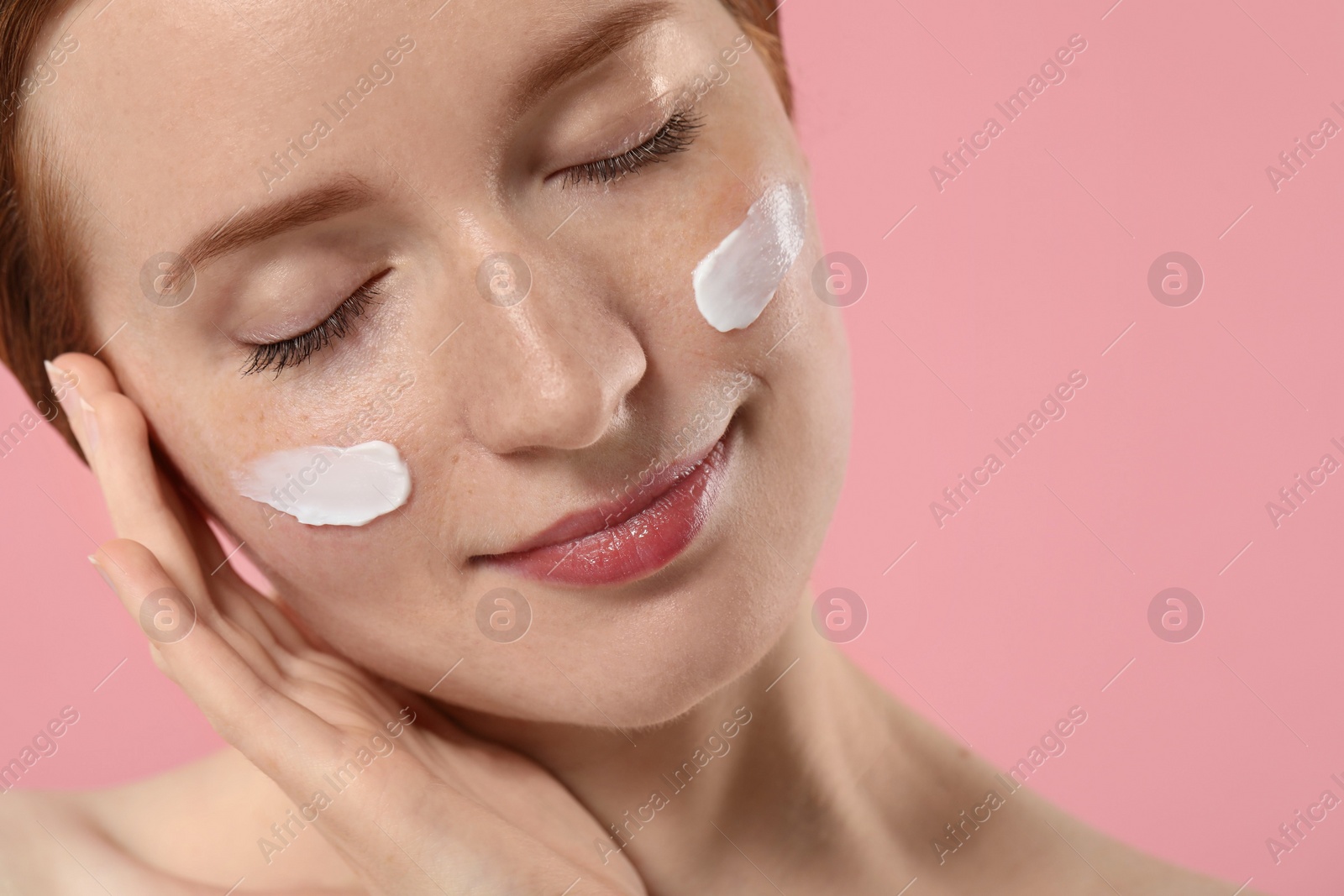 Photo of Beautiful woman with freckles and cream on her face against pink background, closeup. Space for text