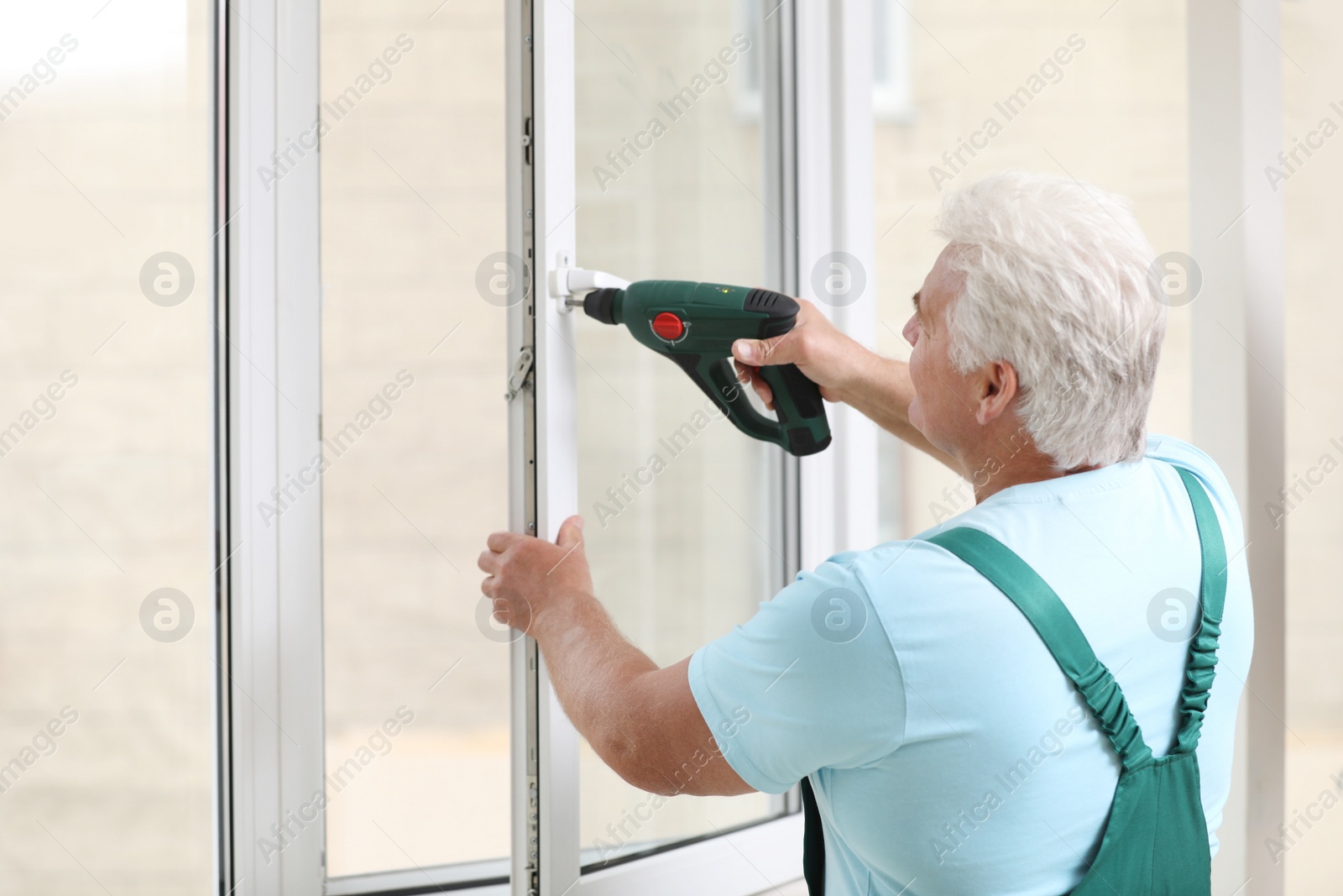 Photo of Mature construction worker repairing plastic window with electric screwdriver indoors