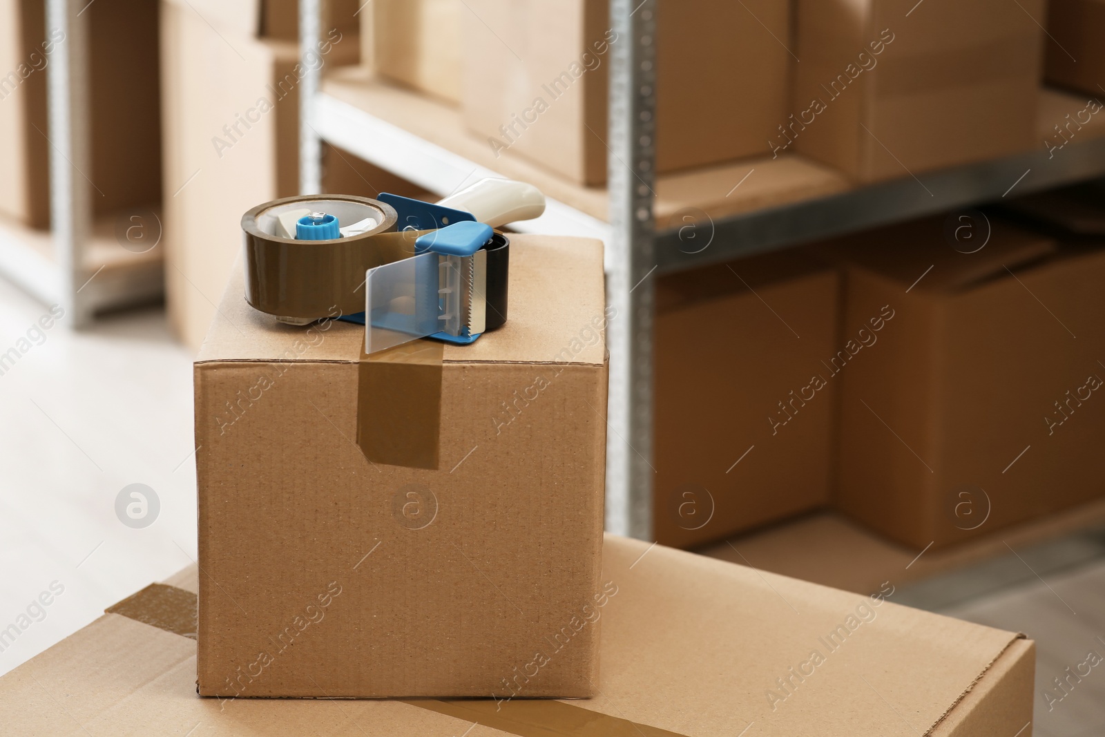 Photo of Adhesive tape dispenser on cardboard box indoors. Space for text