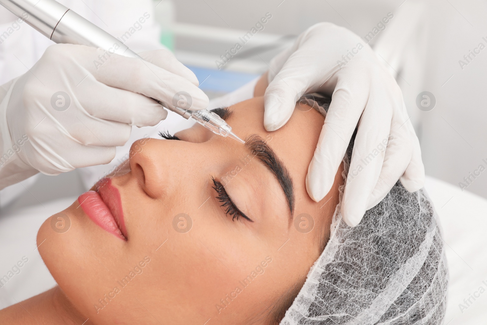 Photo of Young woman undergoing procedure of permanent eyebrow makeup in tattoo salon, closeup