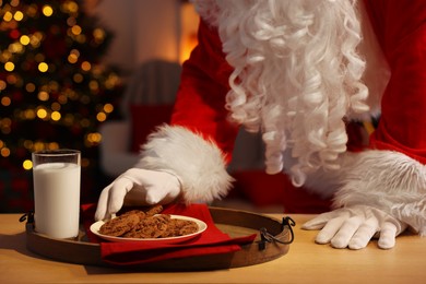 Photo of Merry Christmas. Santa Claus taking cookies from plate on table in room, closeup