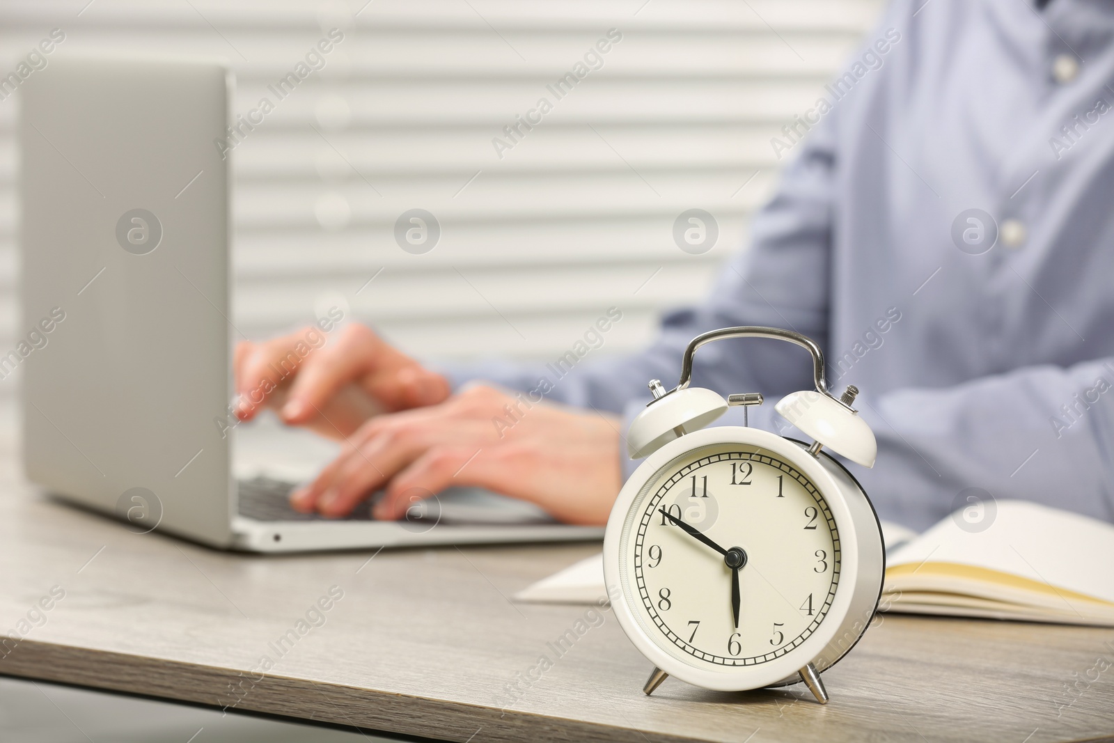 Photo of White alarm clock and man working at wooden table, closeup. Space for text