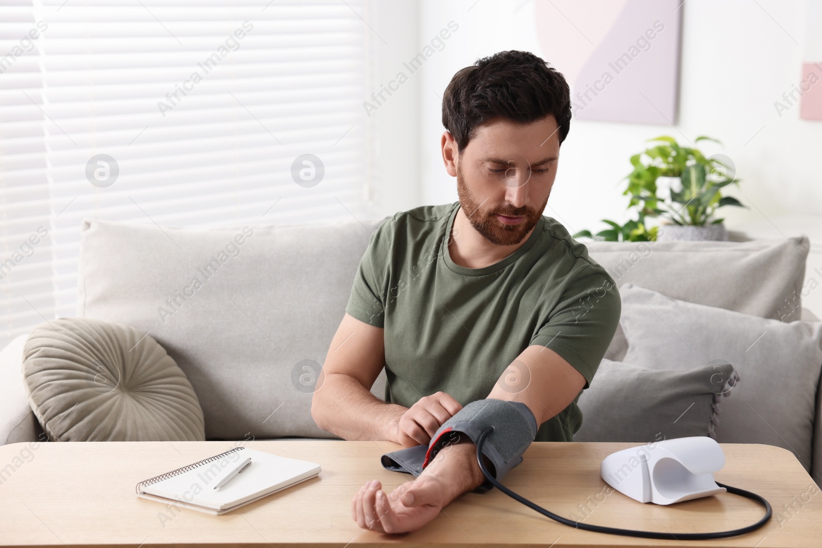 Photo of Man measuring blood pressure at wooden table in room, space for text