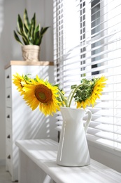 Bouquet of beautiful sunflowers in vase near window at home