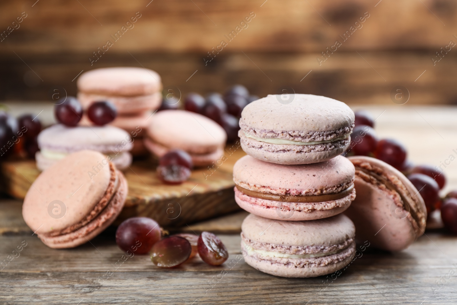 Photo of Delicious macarons and grapes on wooden table. Space for text