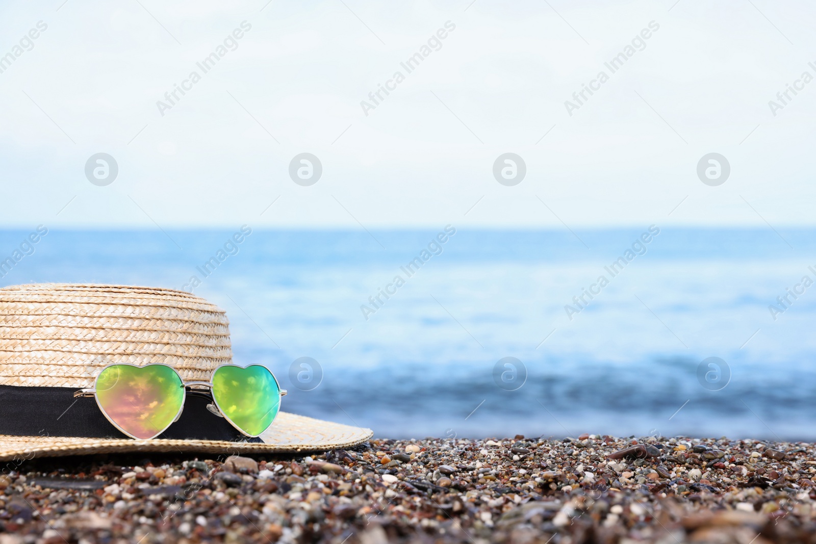 Photo of Straw hat and colorful heart shaped sunglasses on sea beach. Space for text