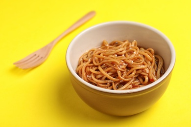 Cooked noodles and wooden fork on yellow background