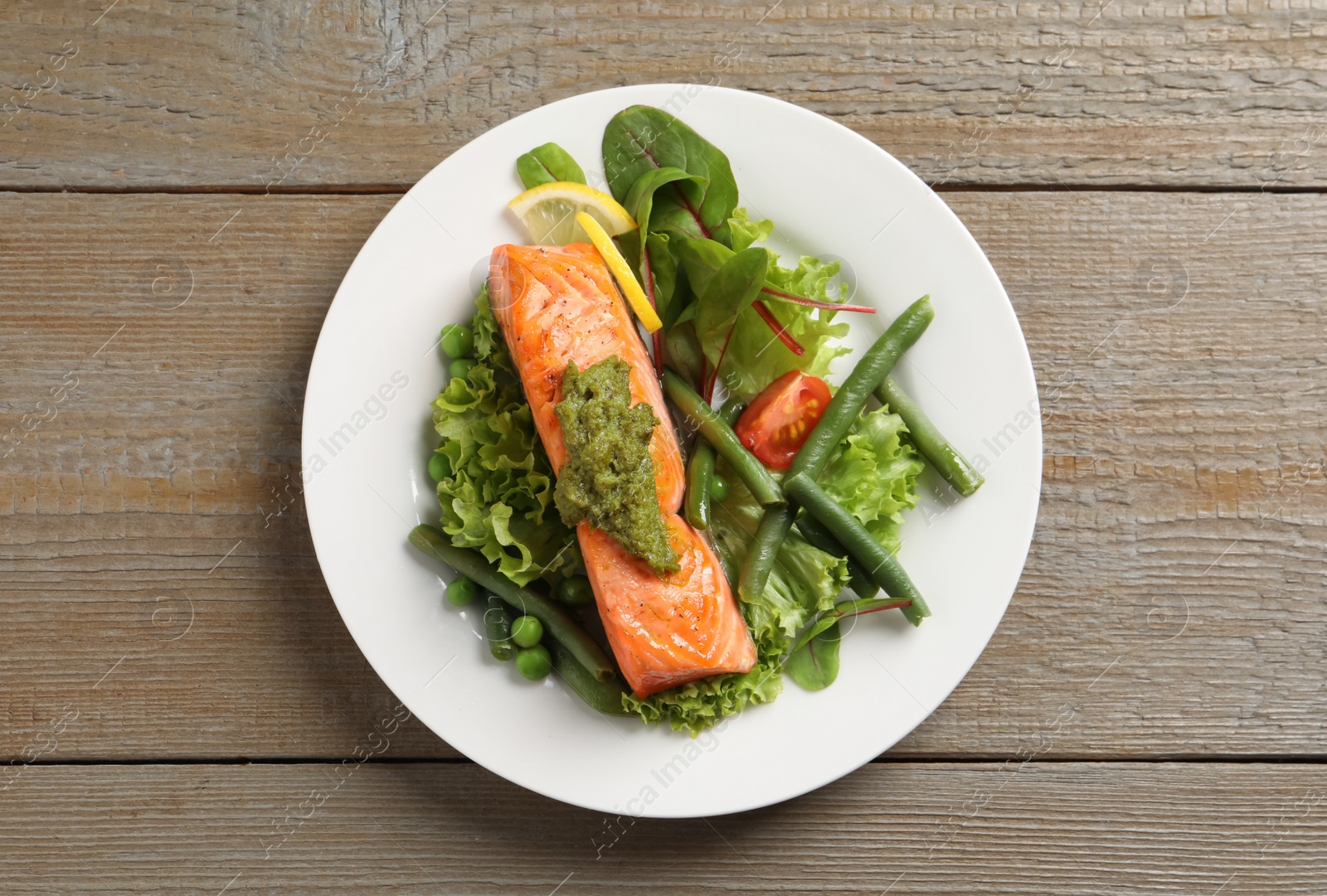 Photo of Tasty cooked salmon with pesto sauce and fresh salad on wooden table, top view