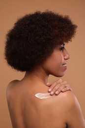 Photo of Beautiful young woman applying body cream onto back on beige background