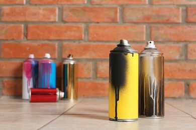 Photo of Used cans of spray paint on floor against brick wall. Space for text